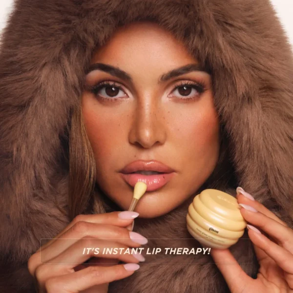 Model in a fur hood applying Honey Glaze Collagen Therapy Lip Mask with its spatula
