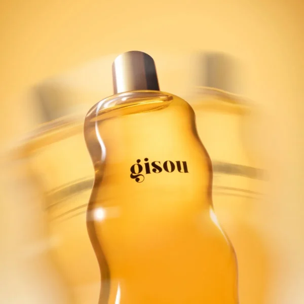 Close-up of the curved Honey Infused Body Oil bottle in warm golden light