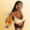 Model holding a bottle of Honey Infused Body Oil against a golden background