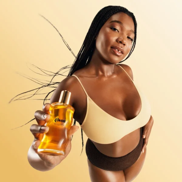 Model holding a bottle of Honey Infused Body Oil against a golden background
