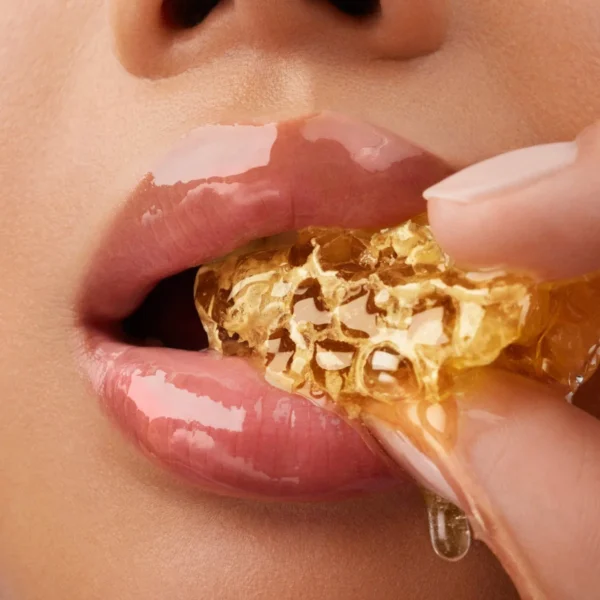 Close-up of glossy lips biting into golden honeycomb